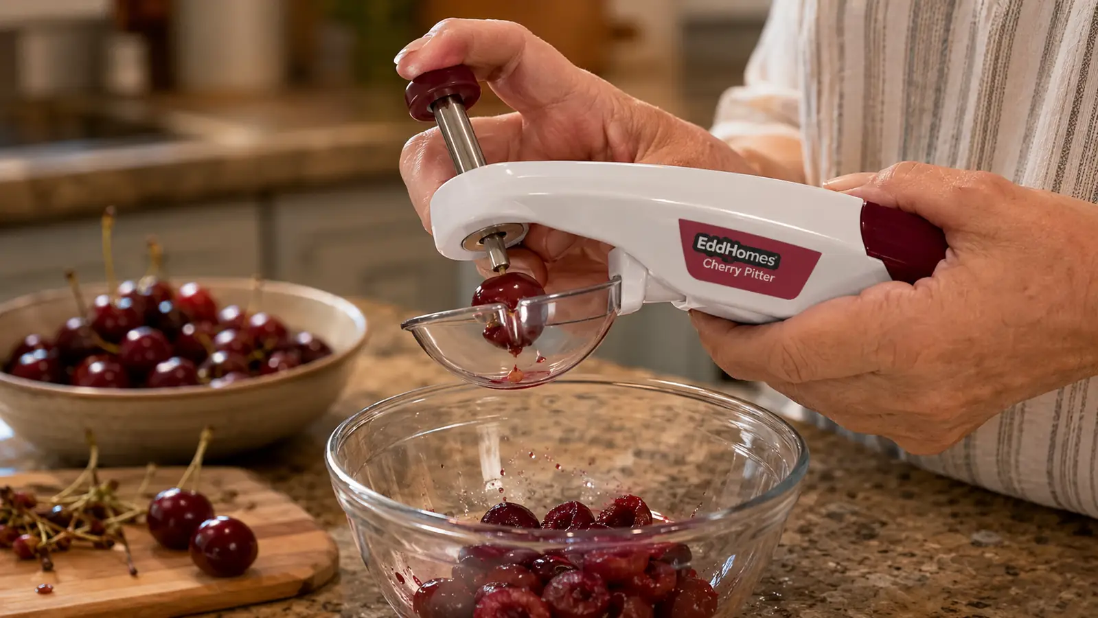 Hand pressing a stainless steel cherry pitter tool over a bowl, pitted cherries falling into the bowl below