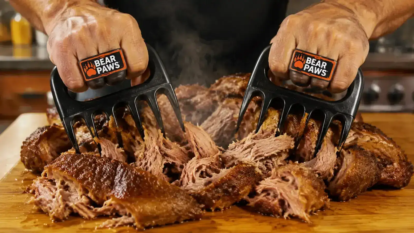 Hands using red-handled bear claw shredders to pull apart a pork shoulder on a cutting board