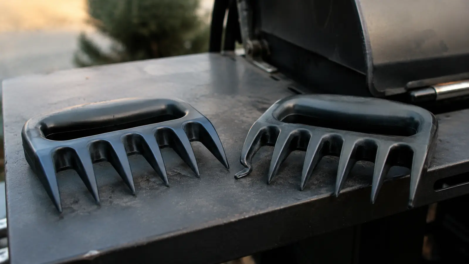 A melted and slightly curled tine on one meat claw sitting on a grill side table next to its undamaged twin