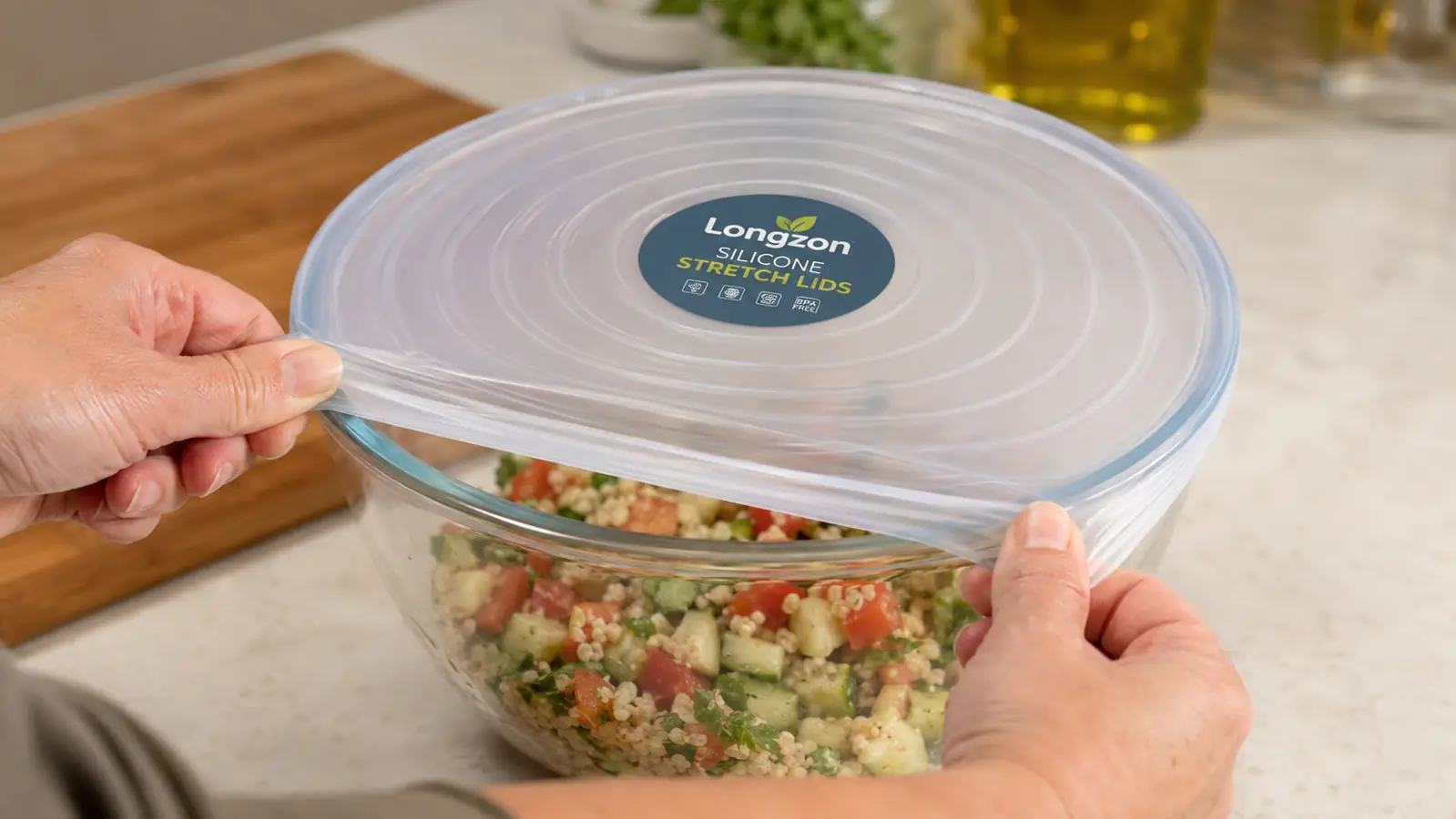 A hand stretching a silicone lid over the top of a mixing bowl filled with leftover pasta