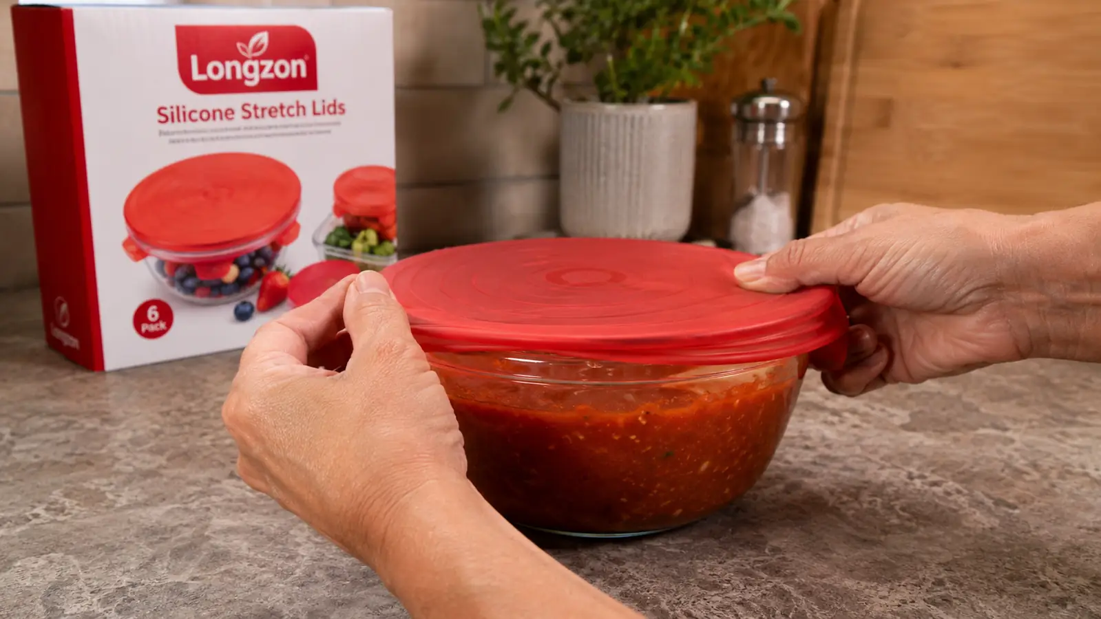A hand stretching a Longzon silicone lid over a bowl of leftover spaghetti sauce