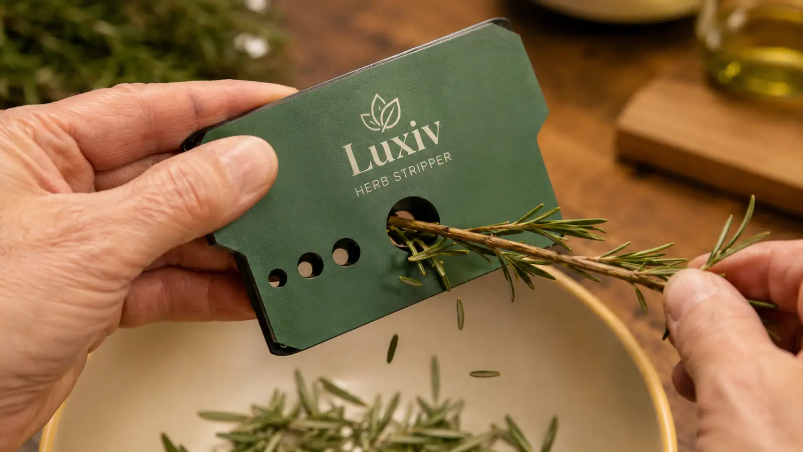 A hand pulling a rosemary sprig through one of the nine holes on the stainless steel herb stripper over a stainless mixing bowl