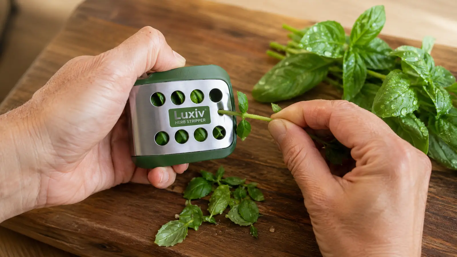Close-up of a hand pulling a thyme stem through the Luxiv stainless steel herb stripper's holes